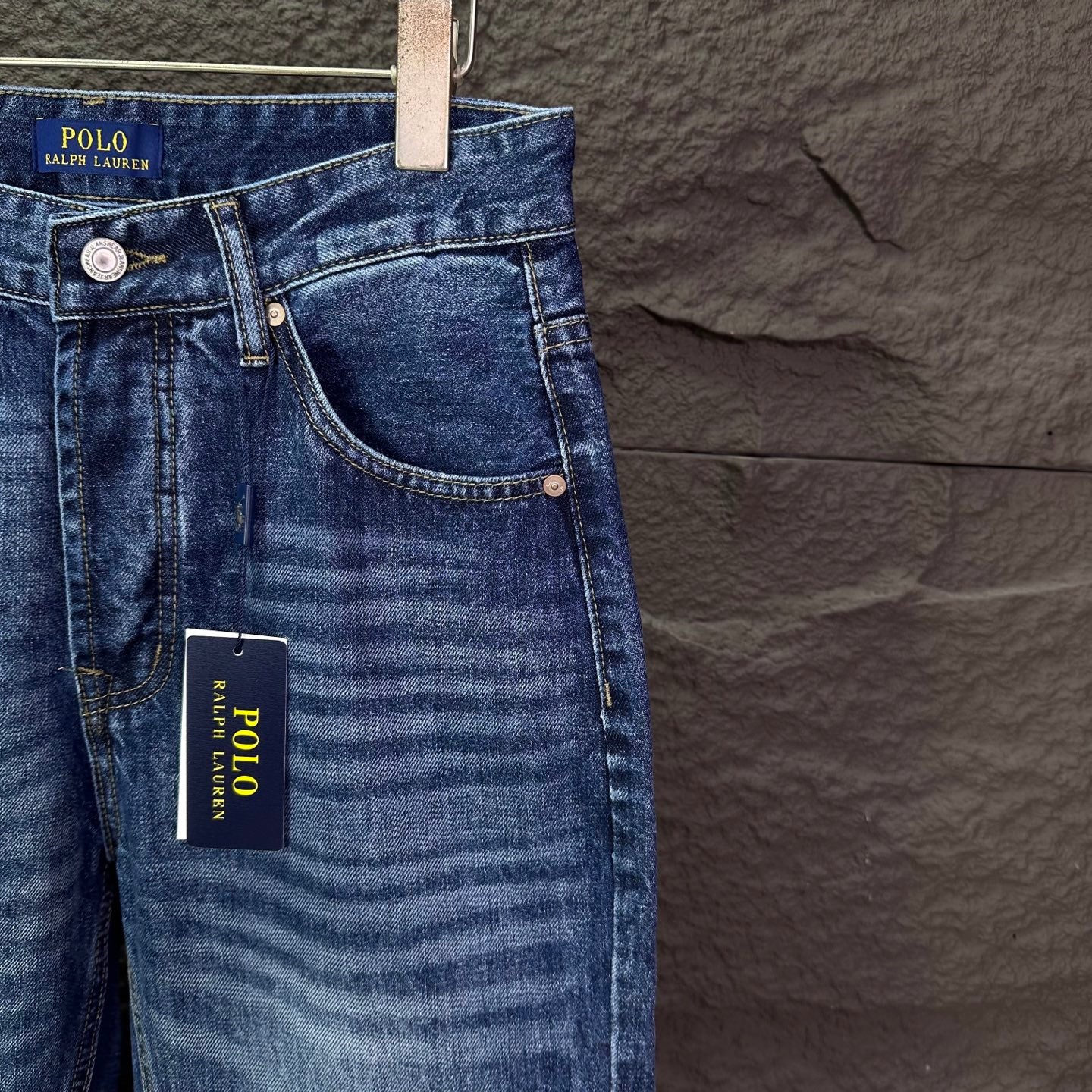 Blue denim jeans front with side pocket and hanging brand tag.