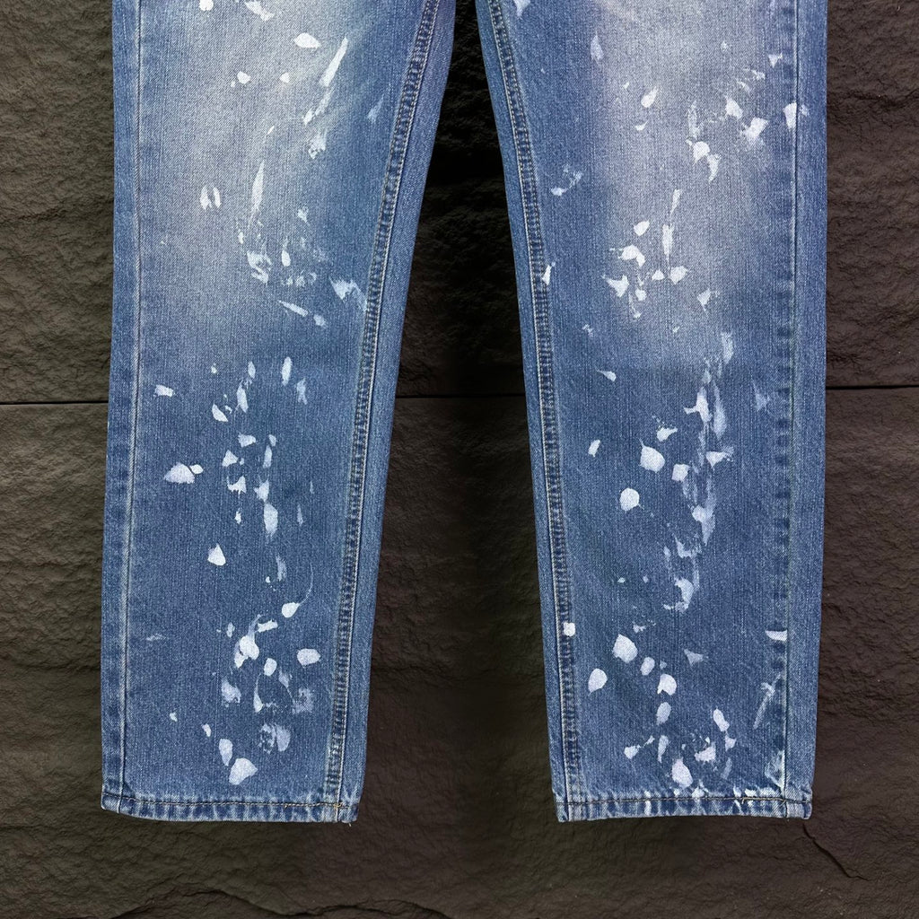 Blue denim jeans leg view with white speckle print, straight hems.
