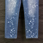 Blue denim jeans leg view with white speckle print, straight hems.