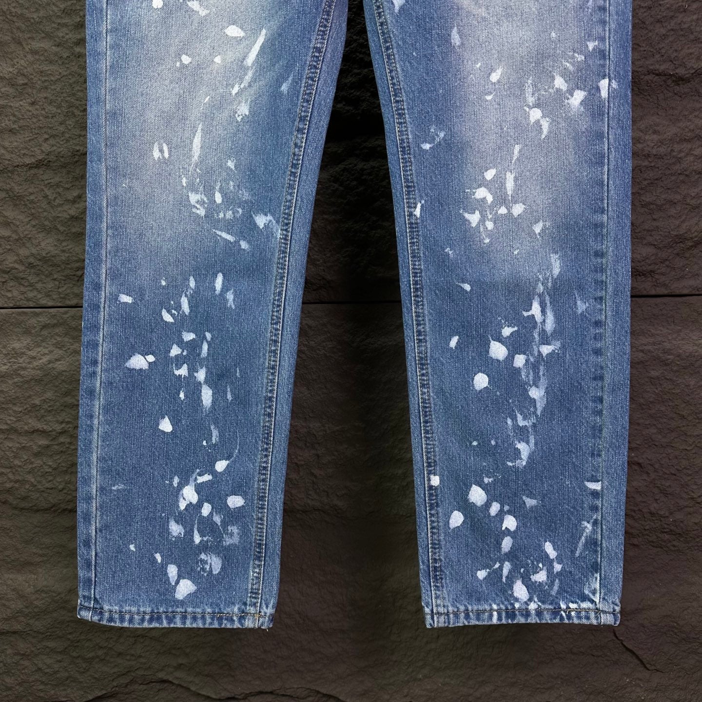 Blue denim jeans leg view with white speckle print, straight hems.
