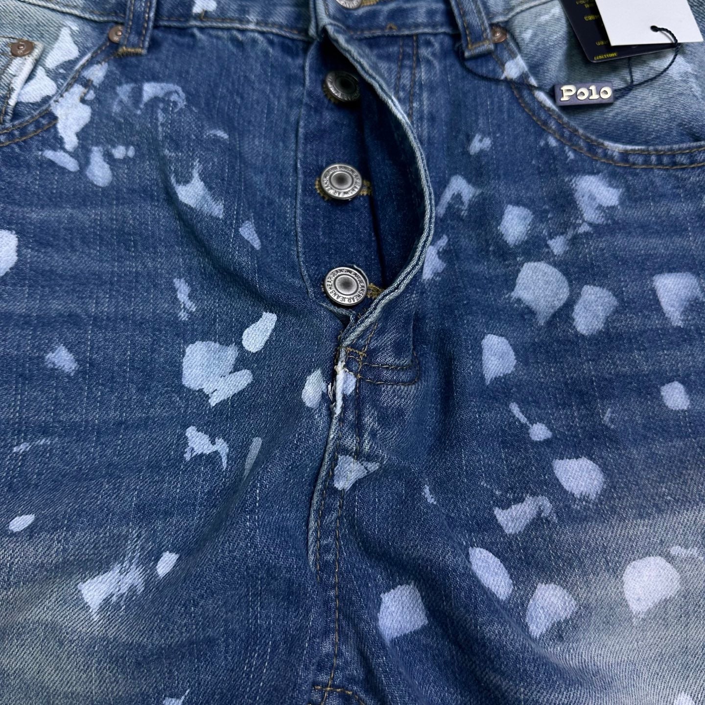 Blue denim jeans close-up of button fly and speckle print, curved pocket seam.