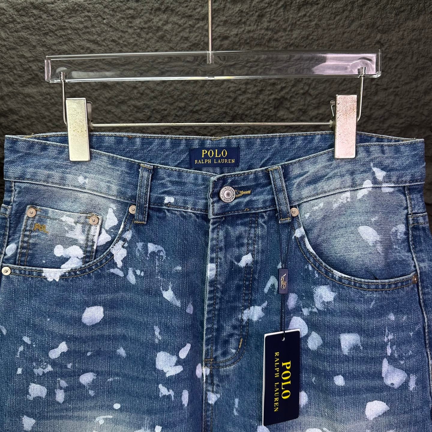 Blue denim jeans waistband with belt loops, button closure, white speckle print.