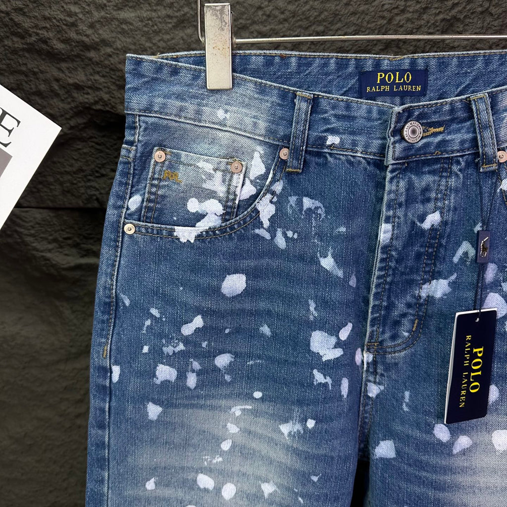 Blue denim jeans with white speckle print, front pockets, brown button accents.