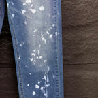 Blue denim jeans side panel with white speckle print and visible seam stitching.