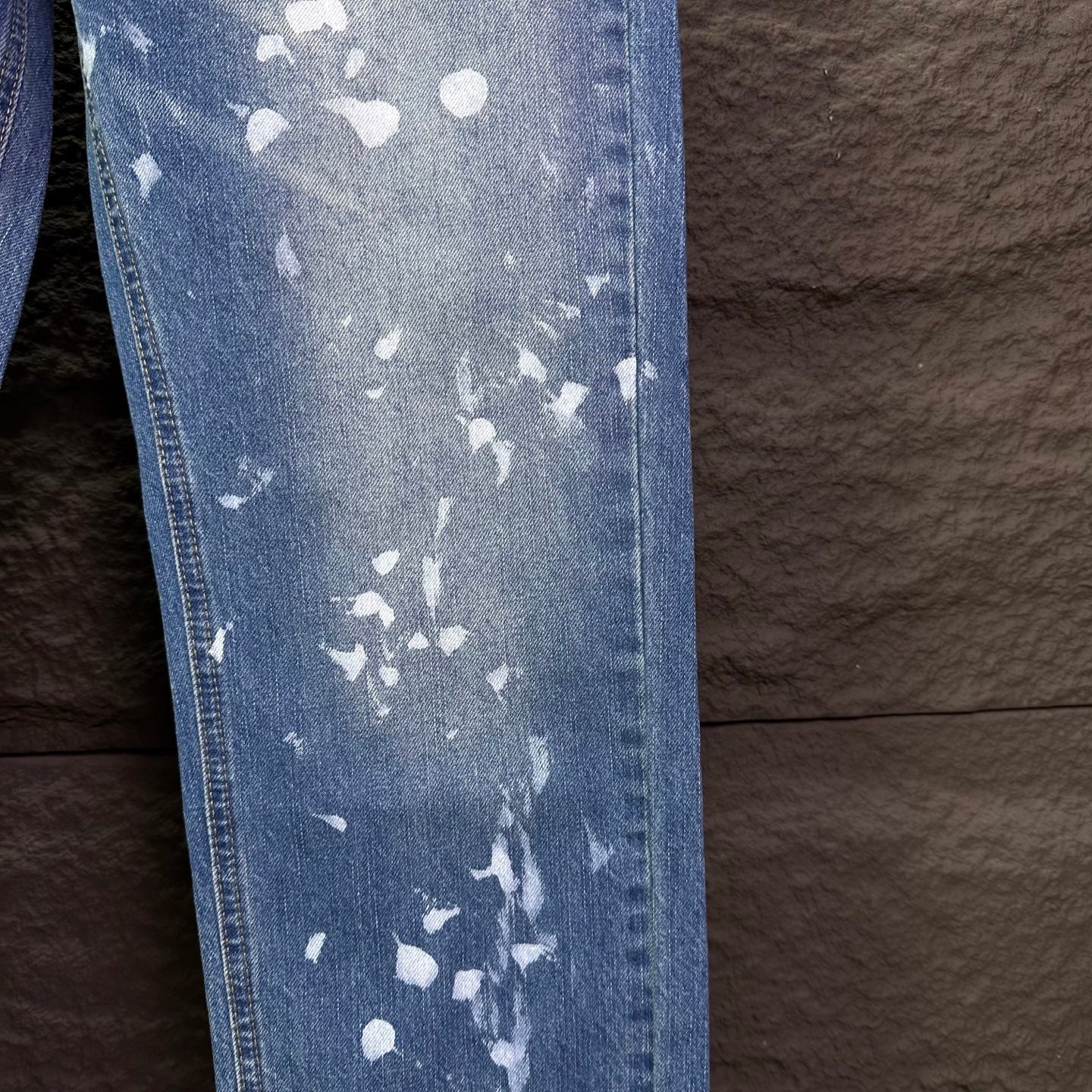 Blue denim jeans side panel with white speckle print and visible seam stitching.