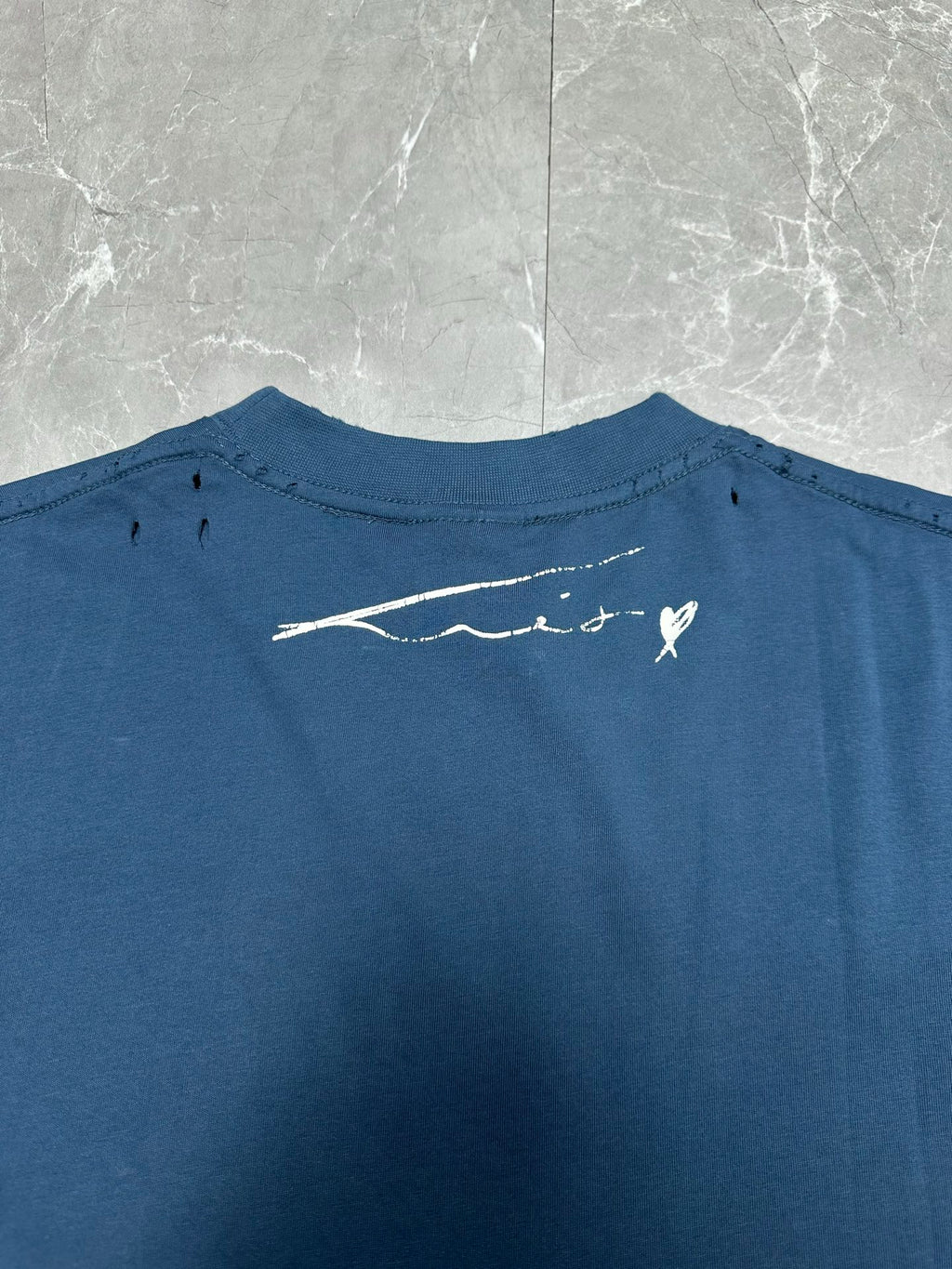 Blue T-shirt back close-up with small white logo signature graphic