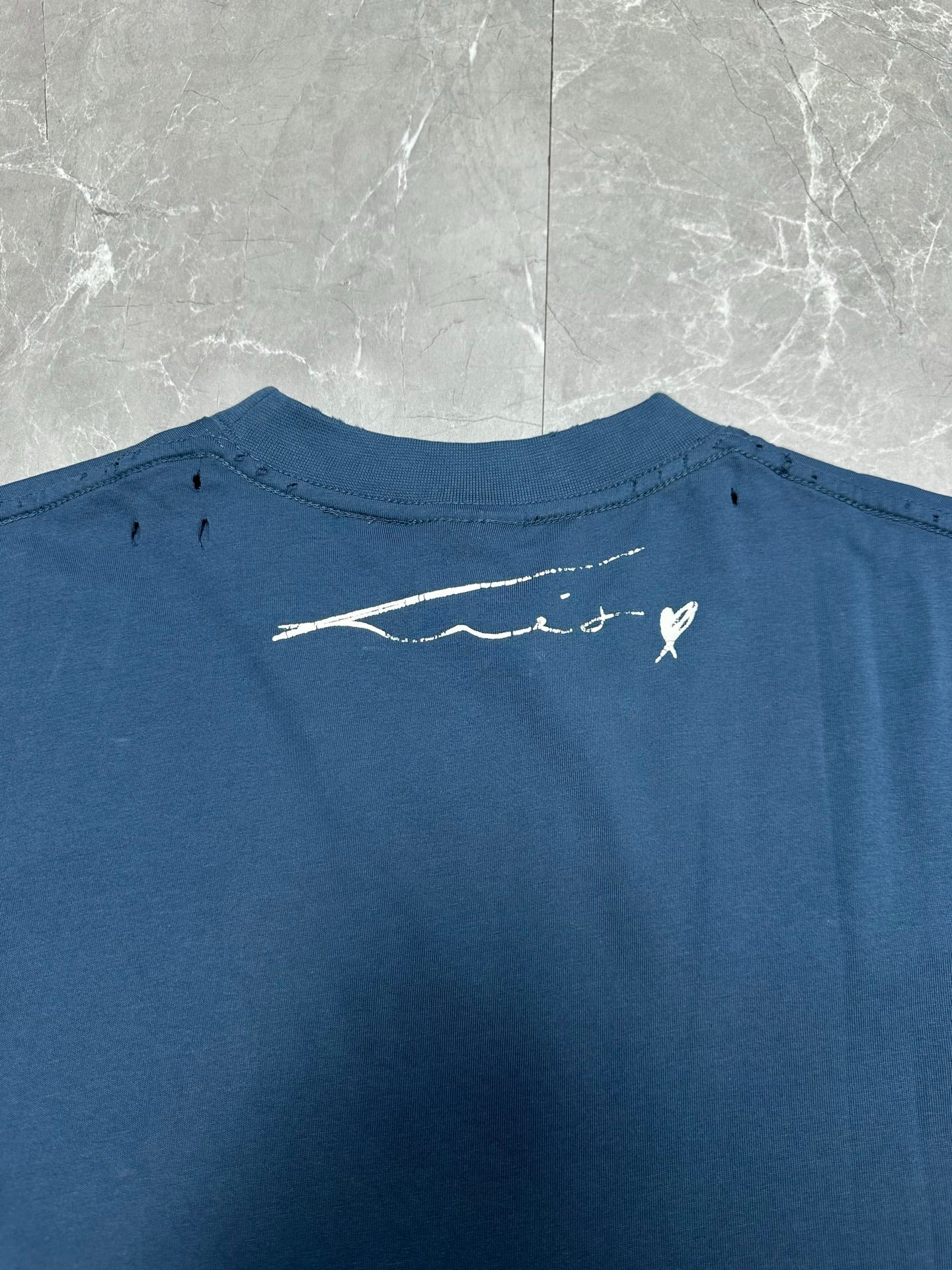 Blue T-shirt back close-up with small white logo signature graphic