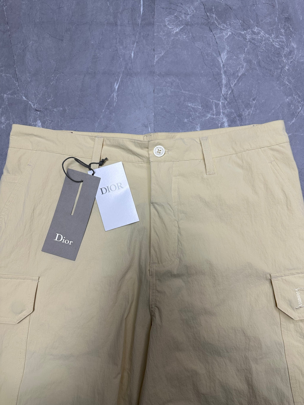 Cream waistband of cargo shorts with button closure and belt loops.