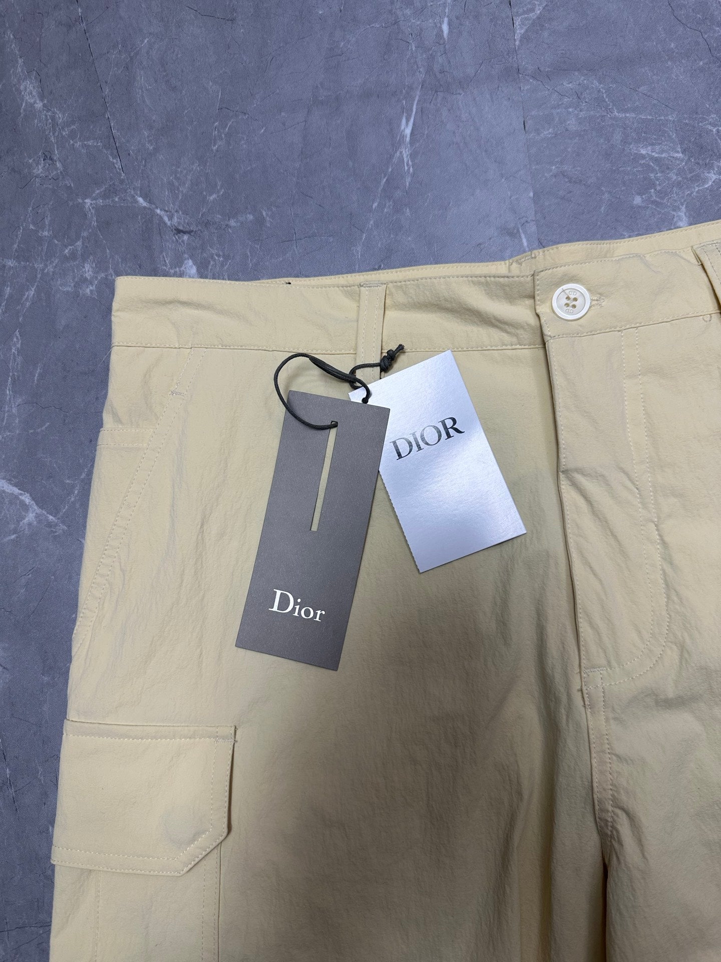 Cream cargo shorts front with button closure, belt loops, and attached tags.