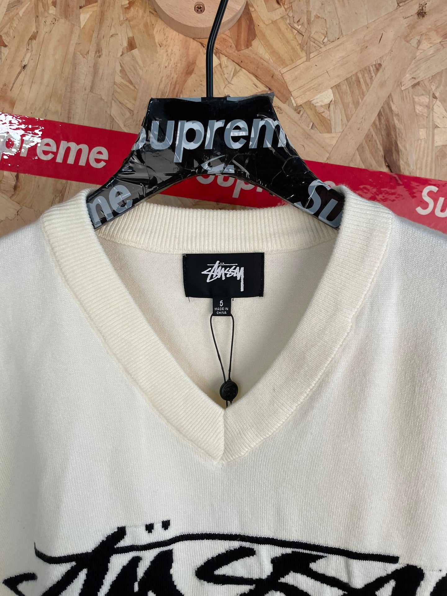 White sleeveless knit vest with V-neck and black Stussy logo graphic, close-up