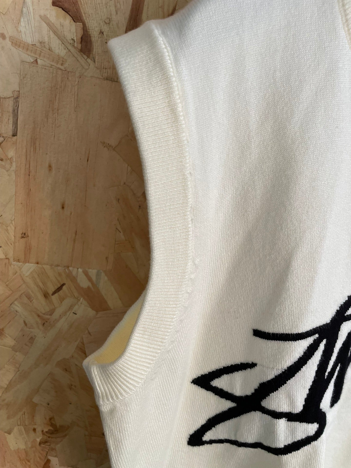 White sleeveless knit vest side with ribbed armhole and partial Stussy graphic