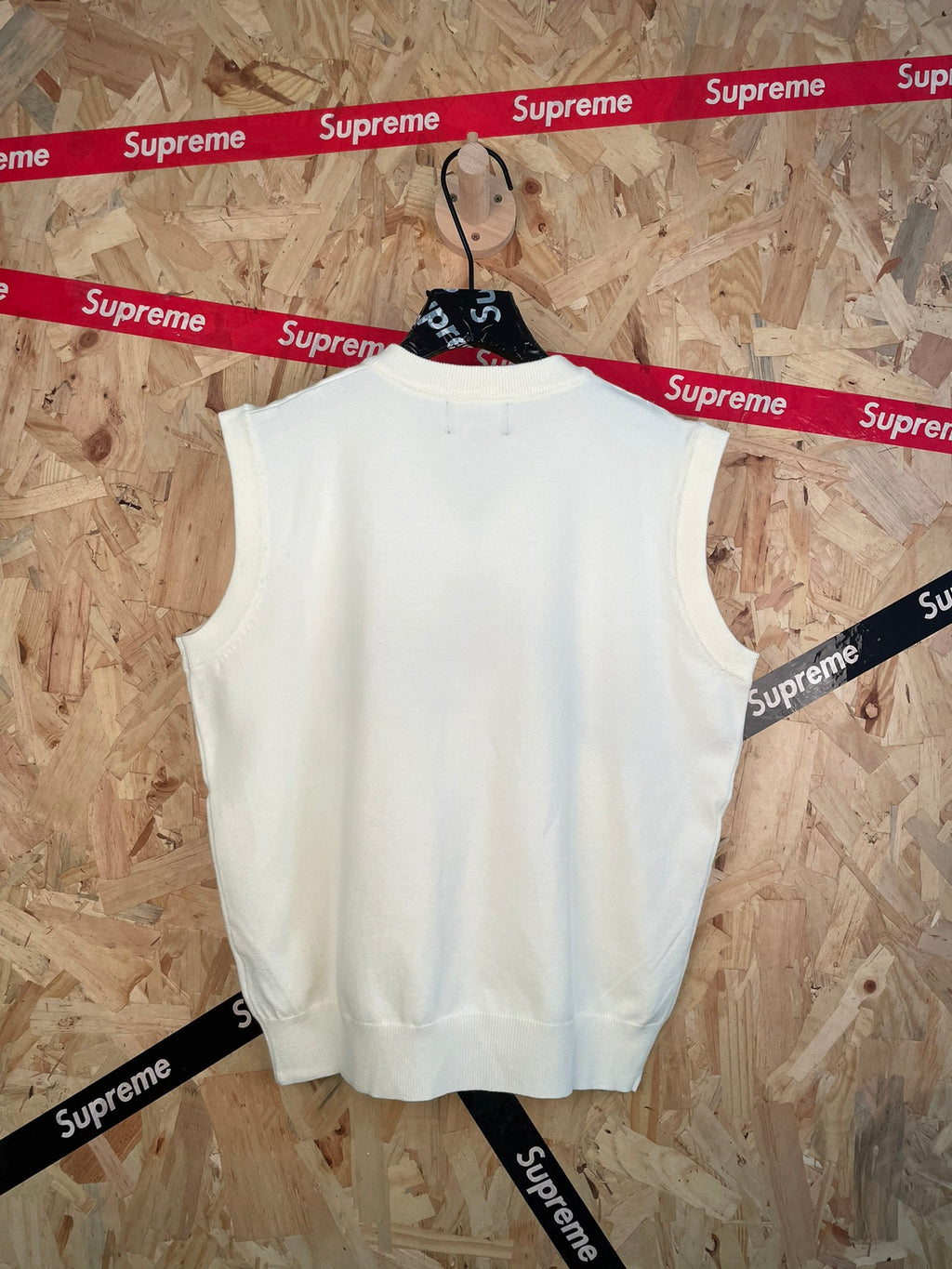 White sleeveless knit vest with V-neck, hanging on a hanger