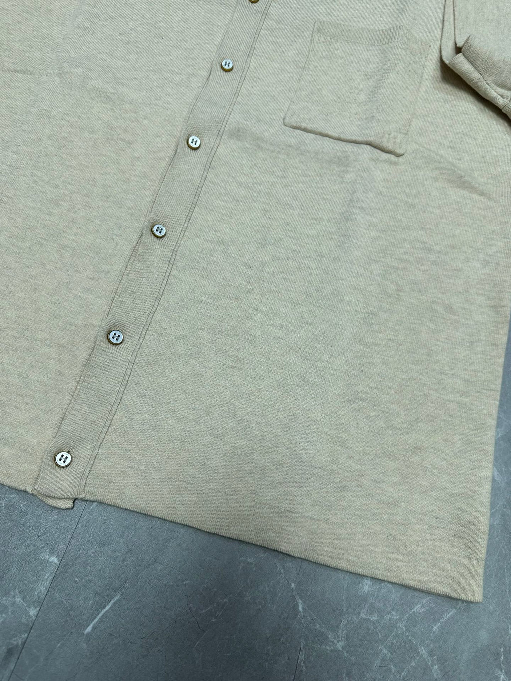 Light beige polo shirt hem and button front, chest pocket panel visible