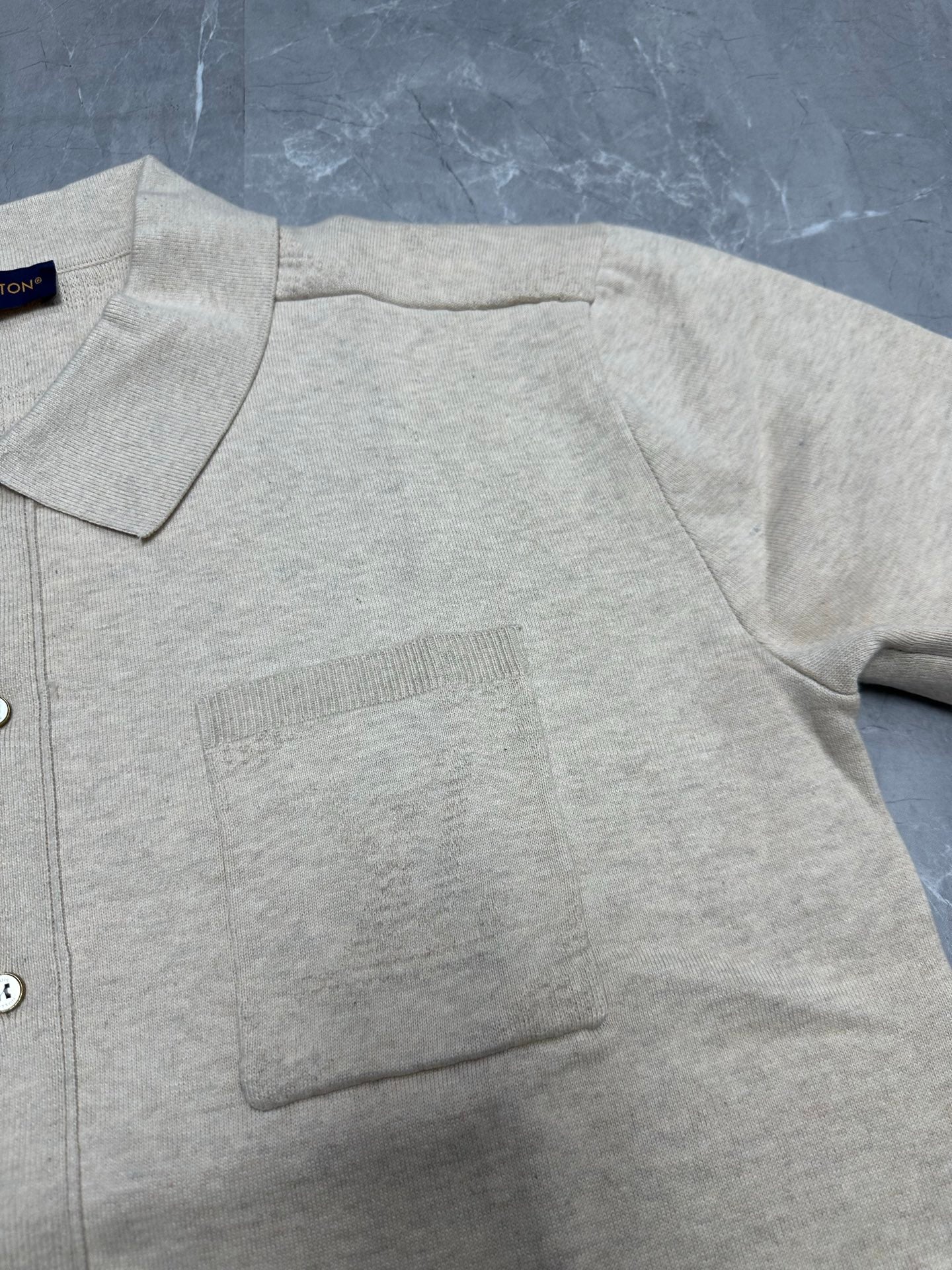 Light beige polo shirt fabric detail, ribbed pocket panel and button placket