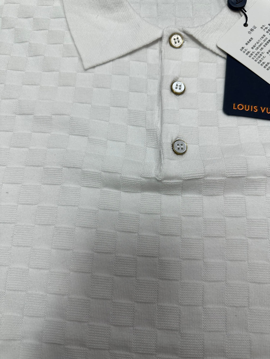 Louis Vuitton white polo shirt detail with tan buttons and embossed textured check