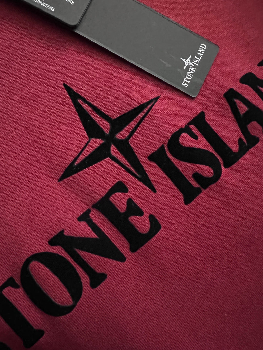 Stone Island sweatshirt fabric close-up with black logo lettering on maroon