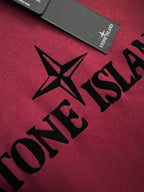 Stone Island sweatshirt fabric close-up with black logo lettering on maroon