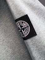 Grey sweatshirt sleeve with black rectangular Stone Island logo patch
