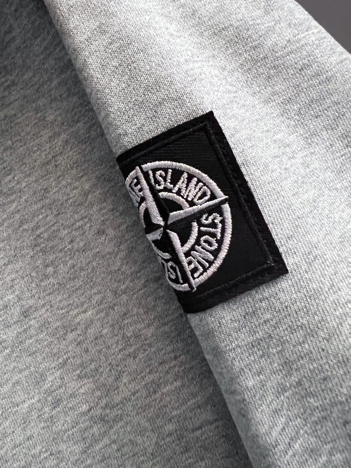 Grey sweatshirt sleeve with black rectangular Stone Island logo patch