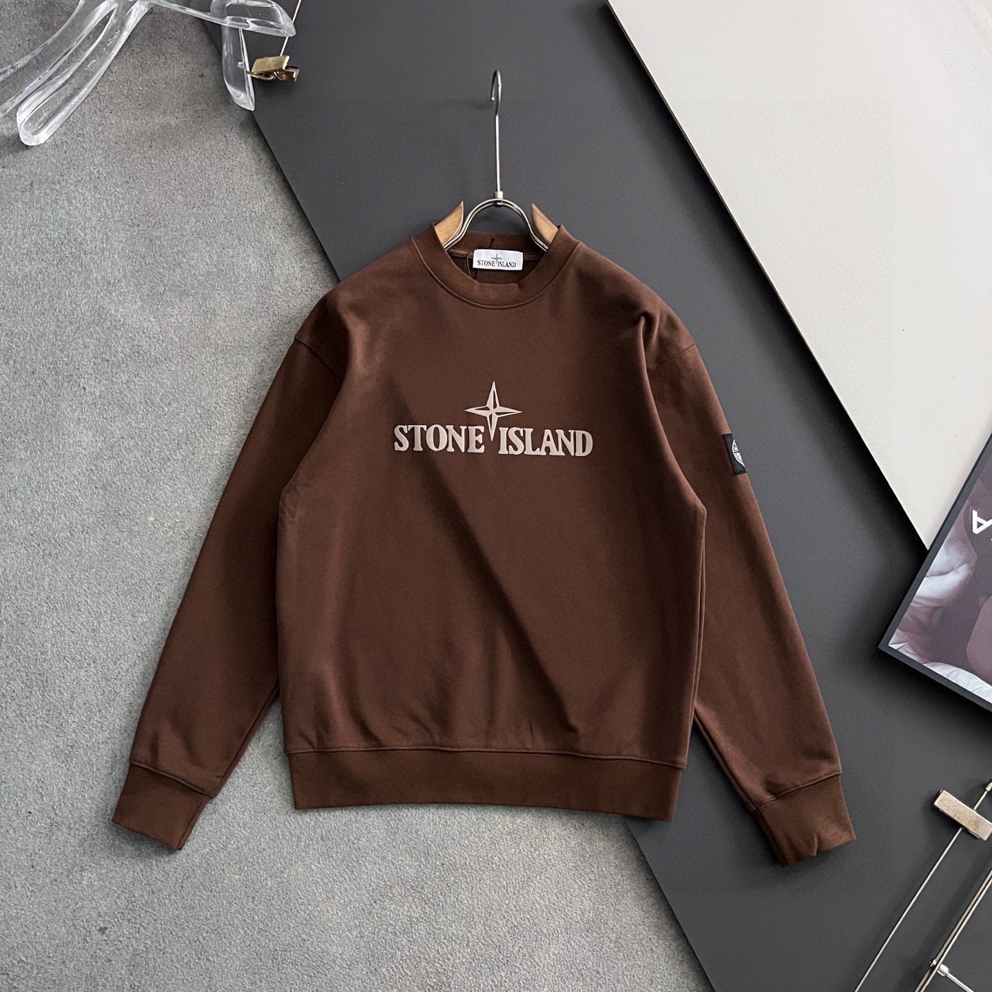 Brown crewneck sweatshirt on hanger with Stone Island chest logo