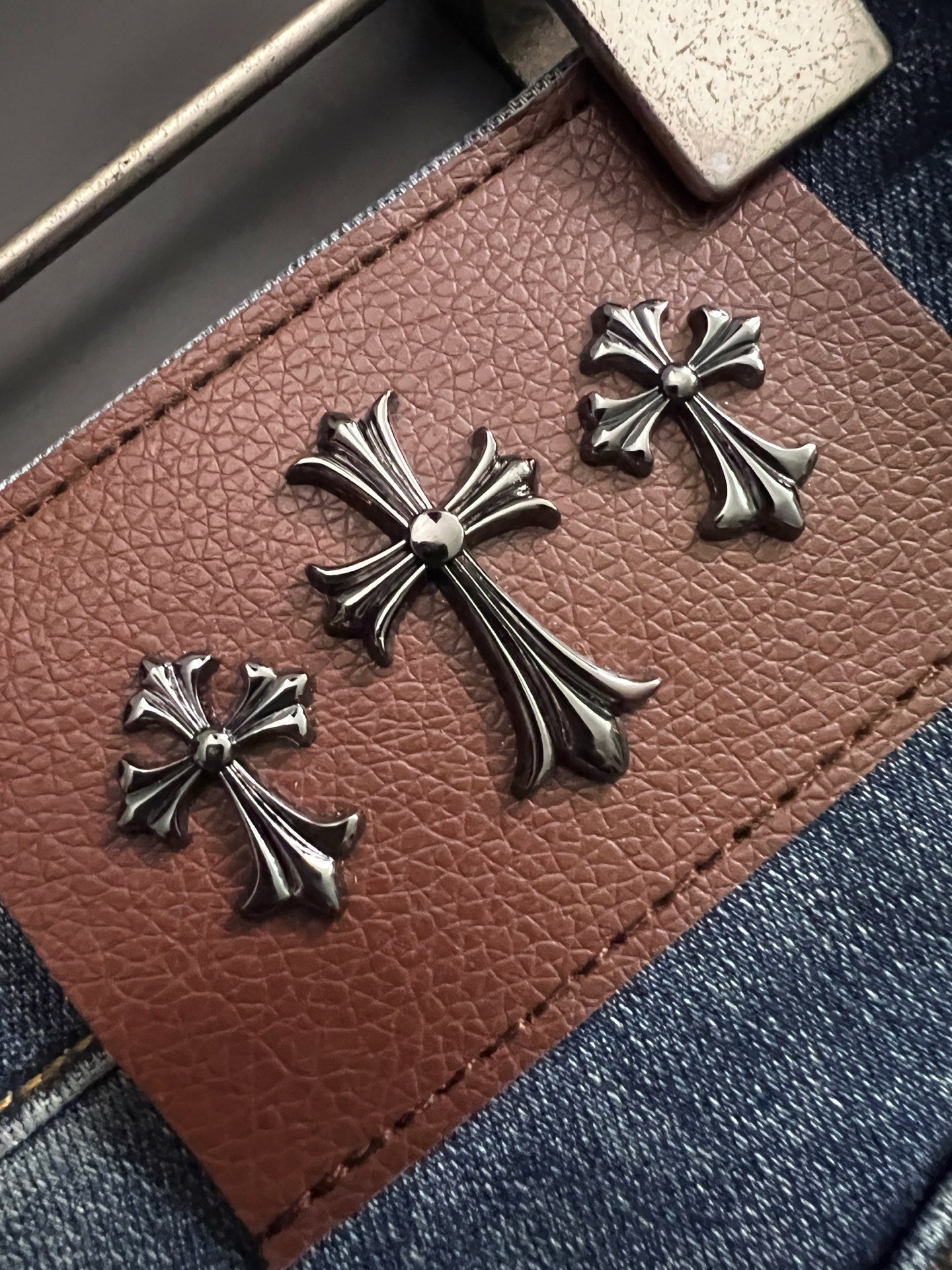 Leather-look patch with cross-like metal charm accents on blue denim