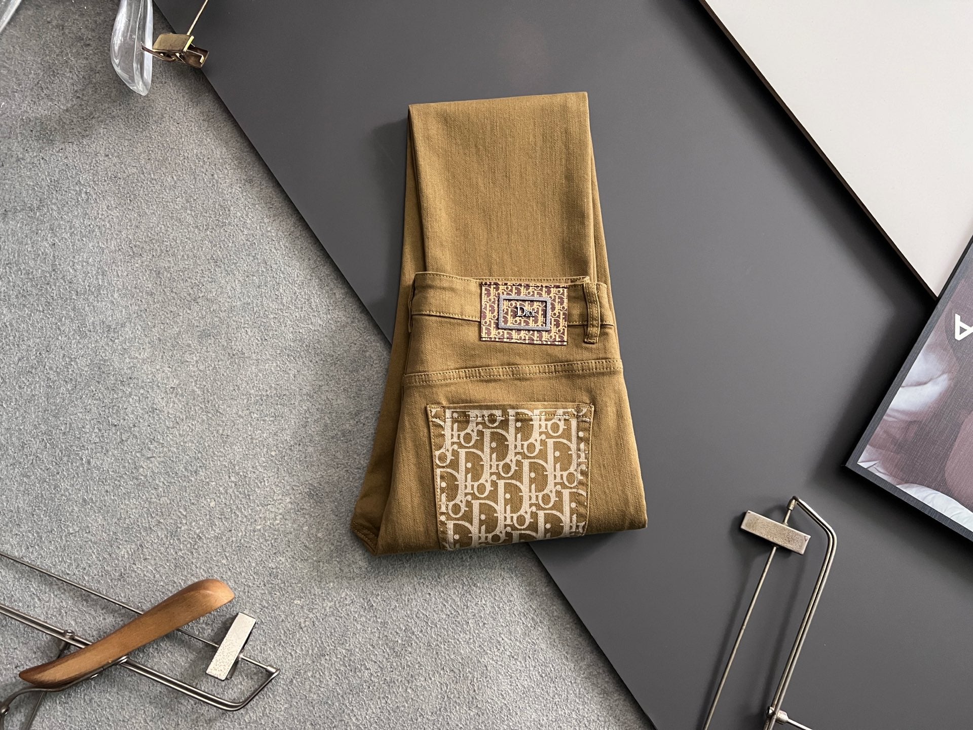 Olive Dior jeans folded on hanger, logo pocket patches shown