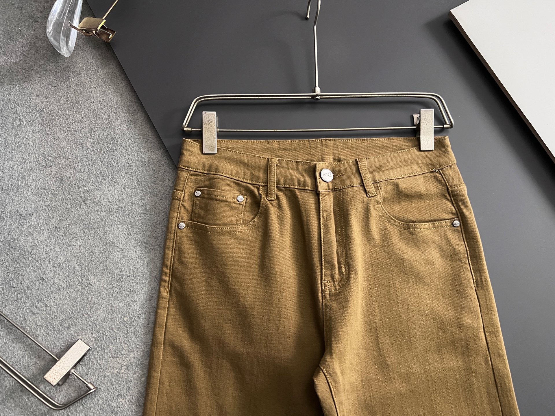 Olive Dior jeans on hanger, front view with belt loops and button
