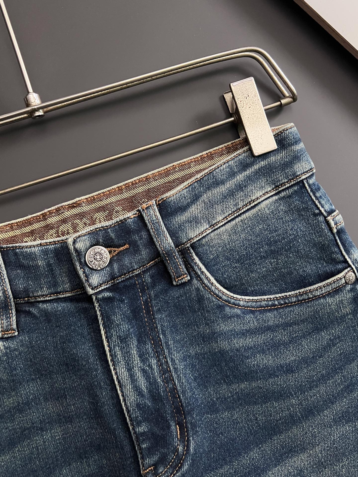 Blue denim jeans front pocket detail with metal button and stitching