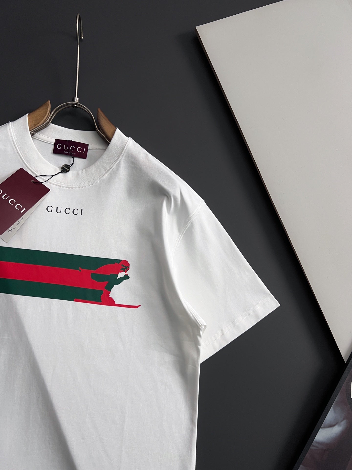 White short-sleeve T-shirt with multicolor stripe and green dog print, angled view