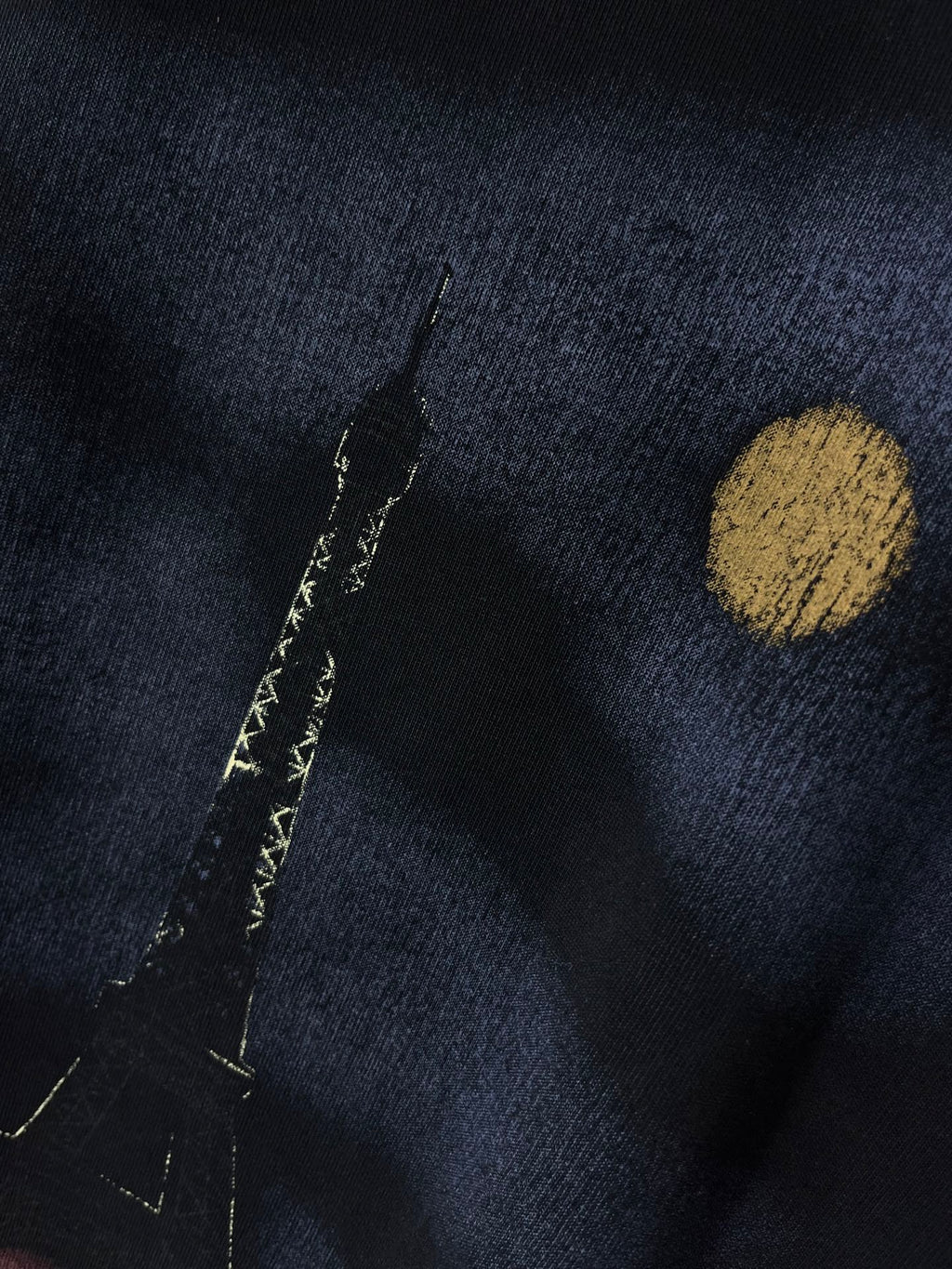 Graphic T-shirt close-up, dark navy fabric with gold dot and vertical marks