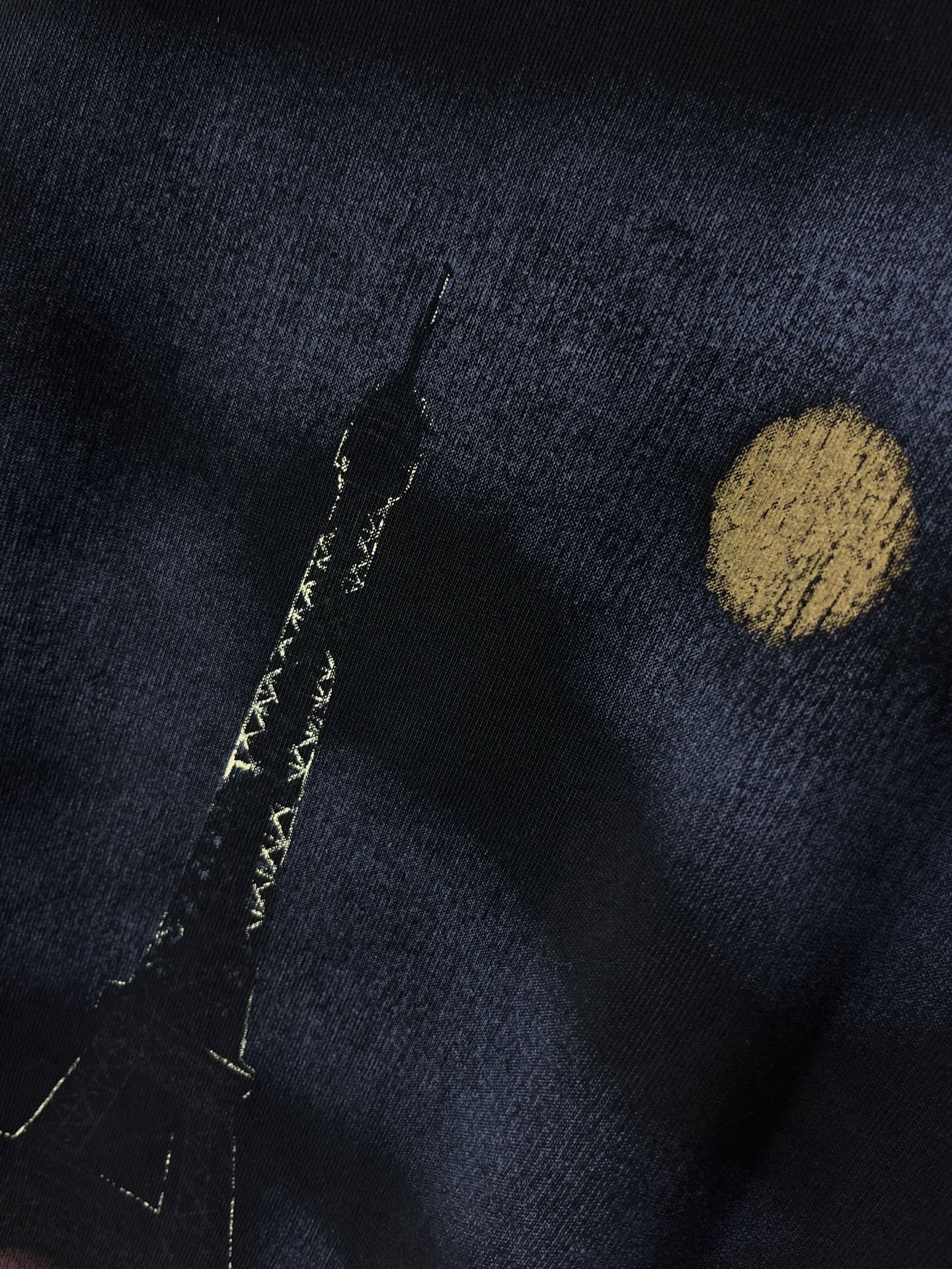 Graphic T-shirt close-up, dark navy fabric with gold dot and vertical marks