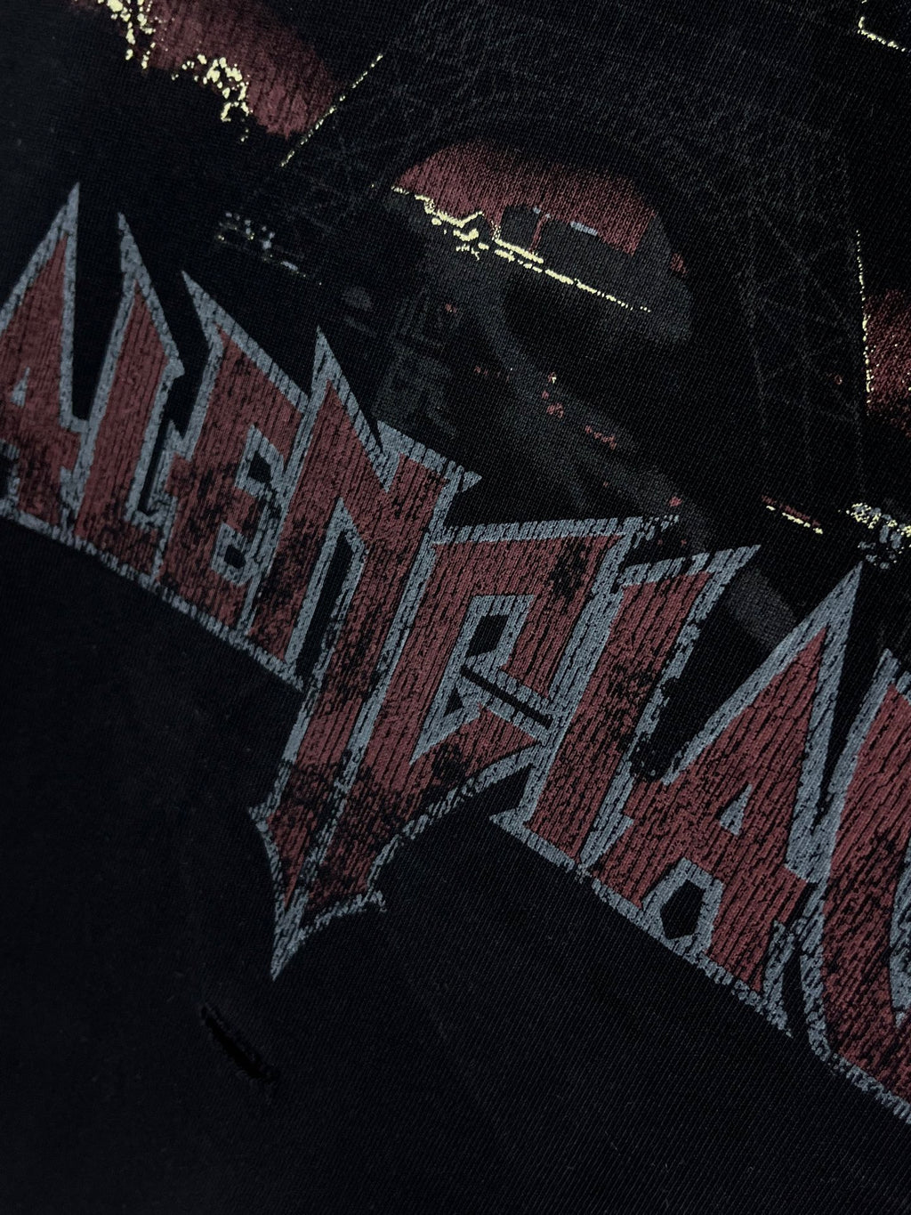 Graphic T-shirt close-up, distressed band-style lettering in red and blue on dark fabric