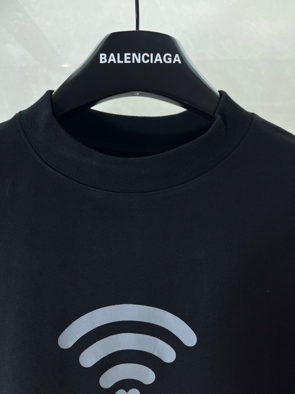 Black T-shirt neckline with small white Wi‑Fi icon and BALENCIAGA chest print