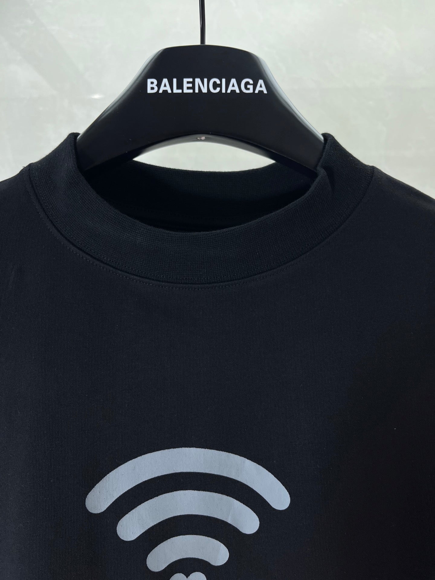 Black T-shirt neckline with small white Wi‑Fi icon and BALENCIAGA chest print