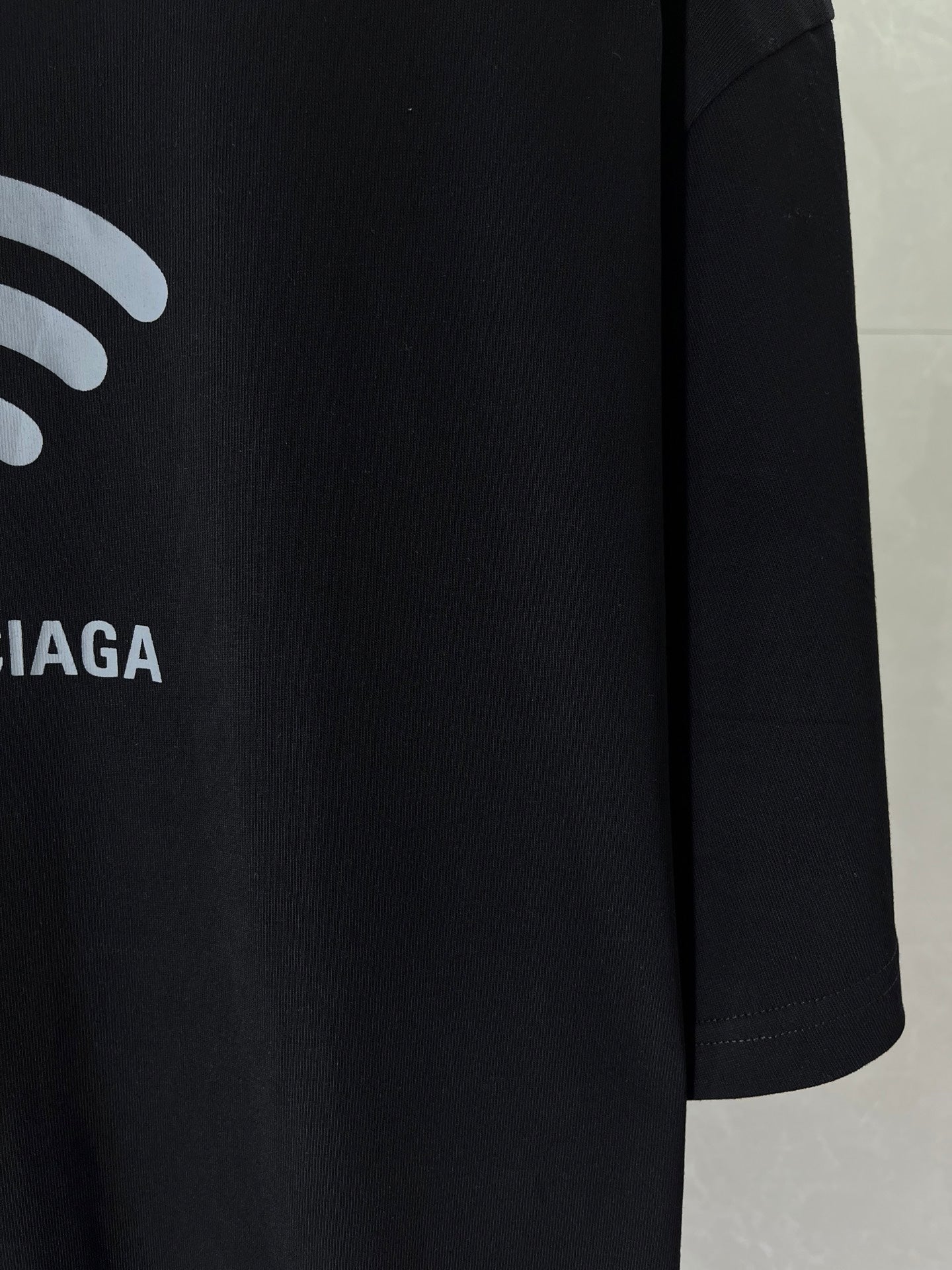 Black T-shirt sleeve detail with white Wi‑Fi icon and partial BALENCIAGA text