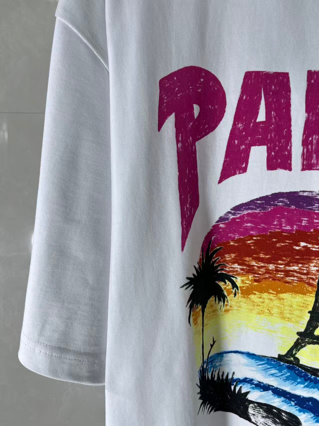 Balenciaga white T-shirt sleeve with partial magenta “PARIS” text and palm art