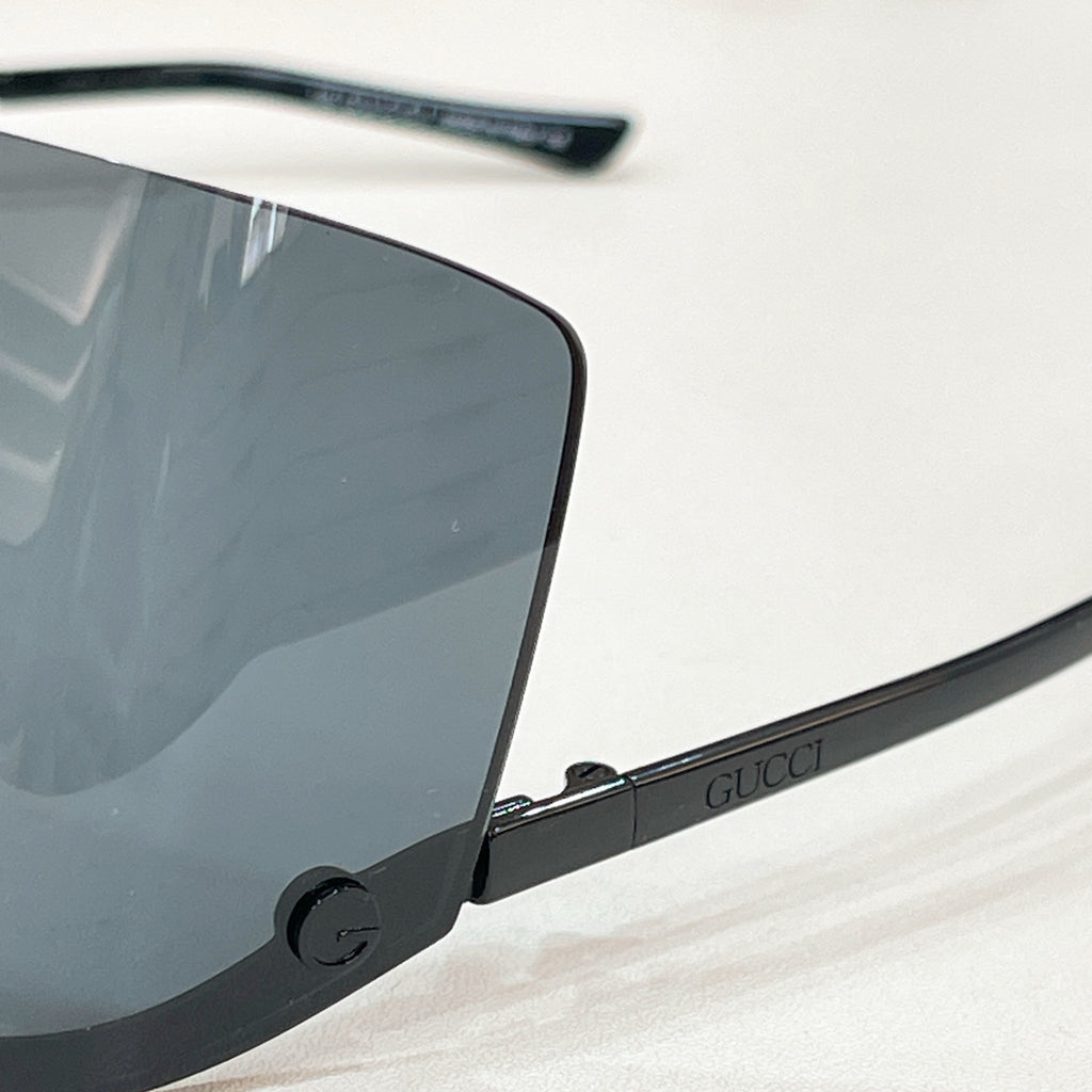 Gucci glasses close-up: black frame with blue tinted lens, gold-tone arm