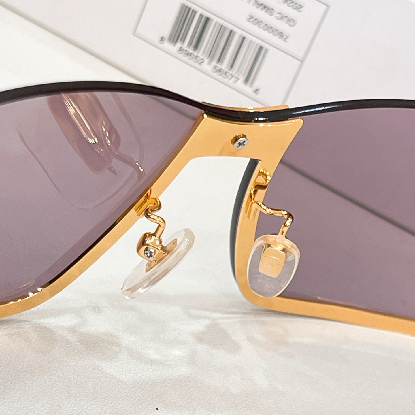 Gucci sunglasses close-up: gold temple arm with small logo and mauve lenses