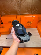 Black slide sandal held in hand, textured crossover strap and flat sole