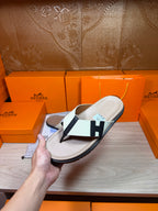 Luxury Hermes slide sandal with cream footbed, white strap, black H buckle detail