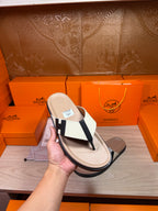 Luxury Hermes sandal held up, cream footbed with white strap and black H buckle