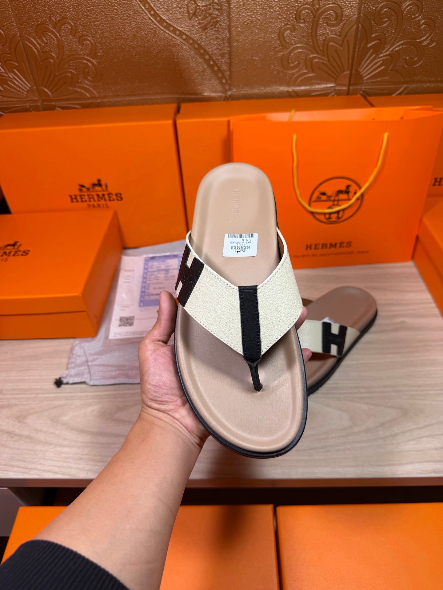 Luxury Hermes sandal close-up on cream footbed with white strap and black H buckle