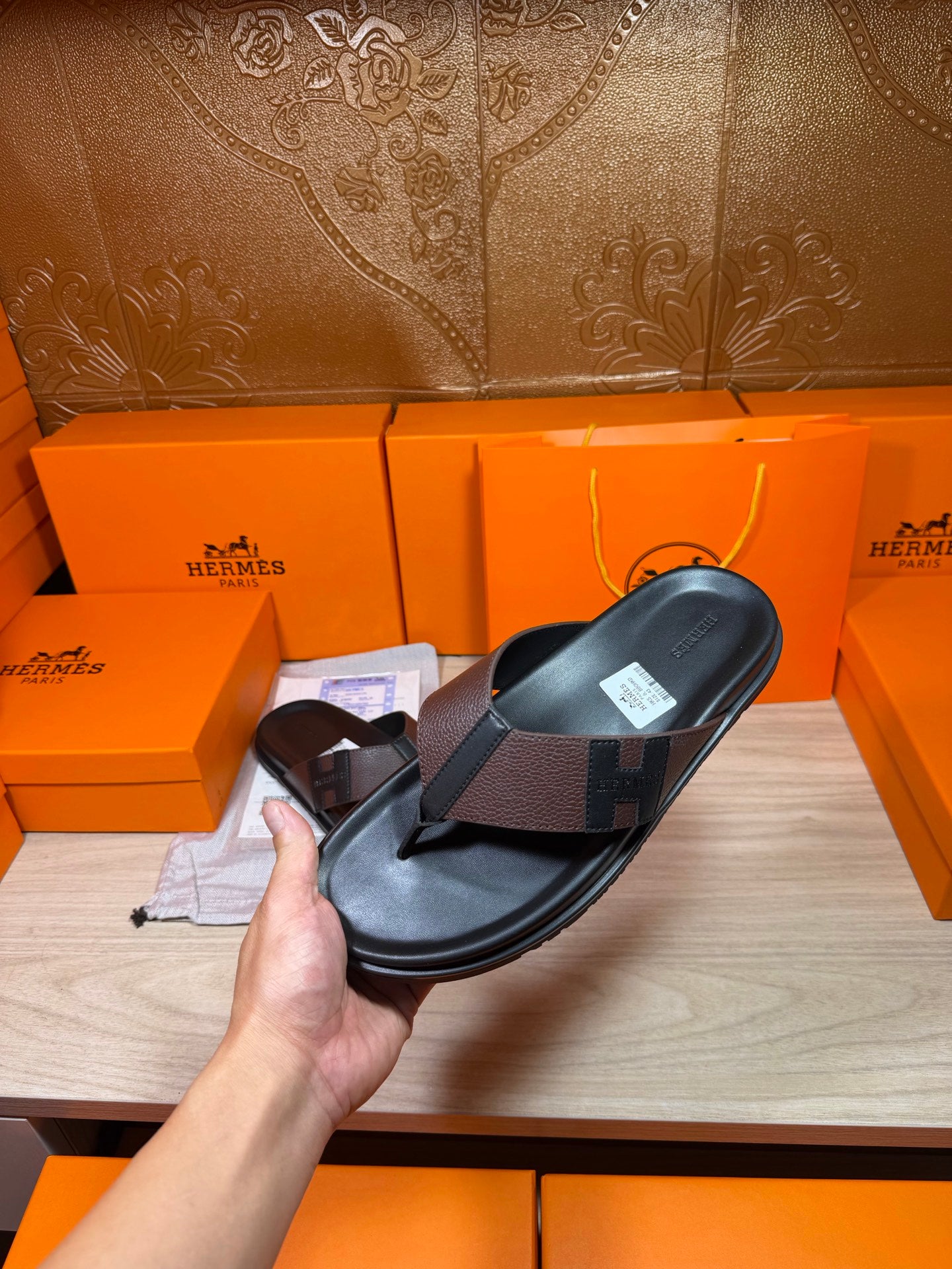 Hand holding black leather thong sandal with textured crossover strap and footbed