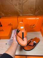 Orange Hermes thong sandals with black H strap shown in hand