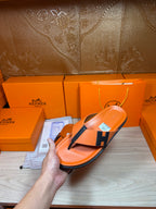 Orange Hermes flip-flop sandals with black H logo strap and curved toe thong