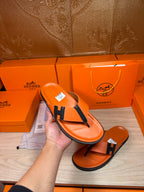 Hand holding orange Hermes flip-flop sandals with black H thong strap