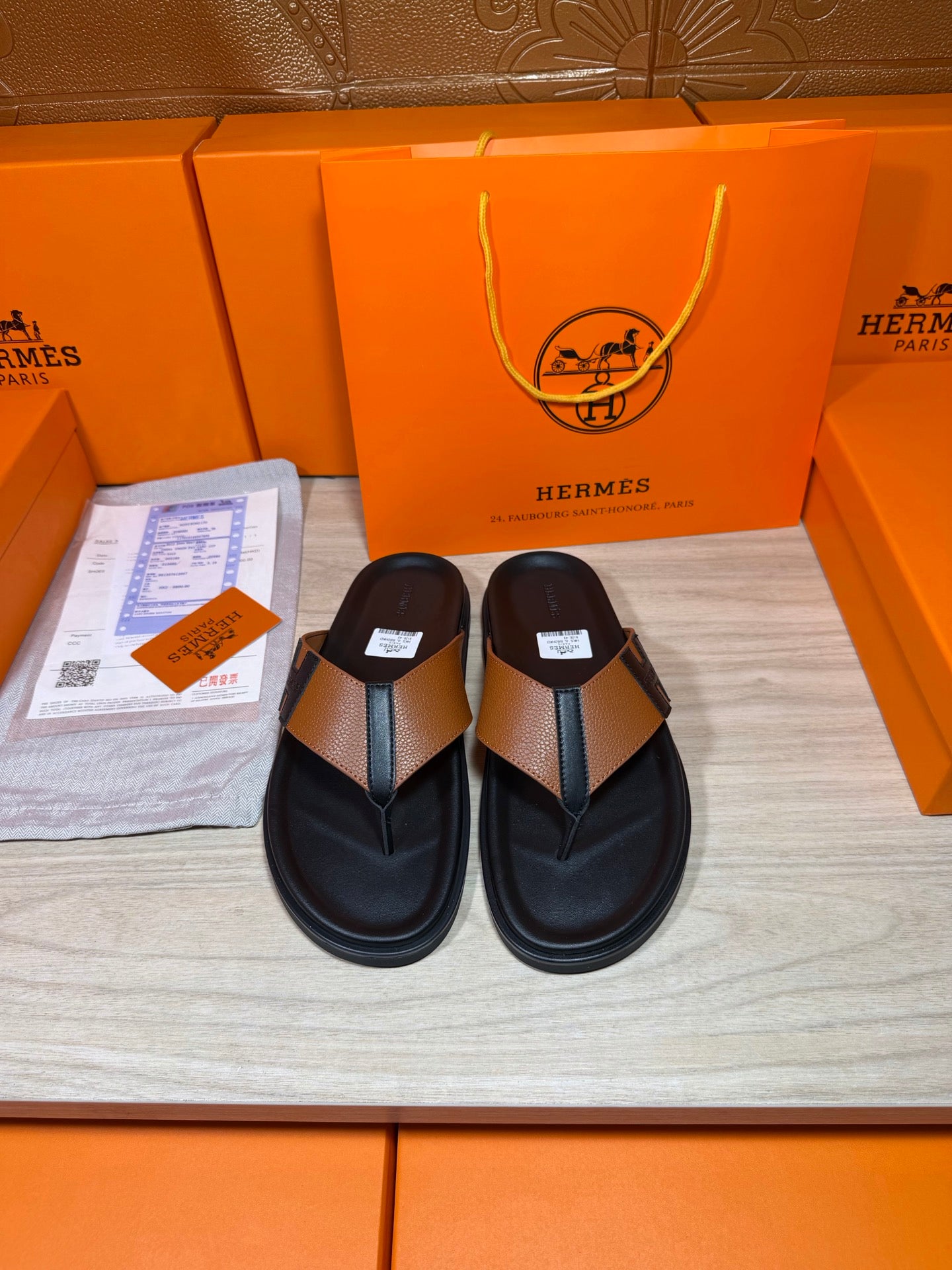 Pair of black thong sandals with tan strap and H buckle detail