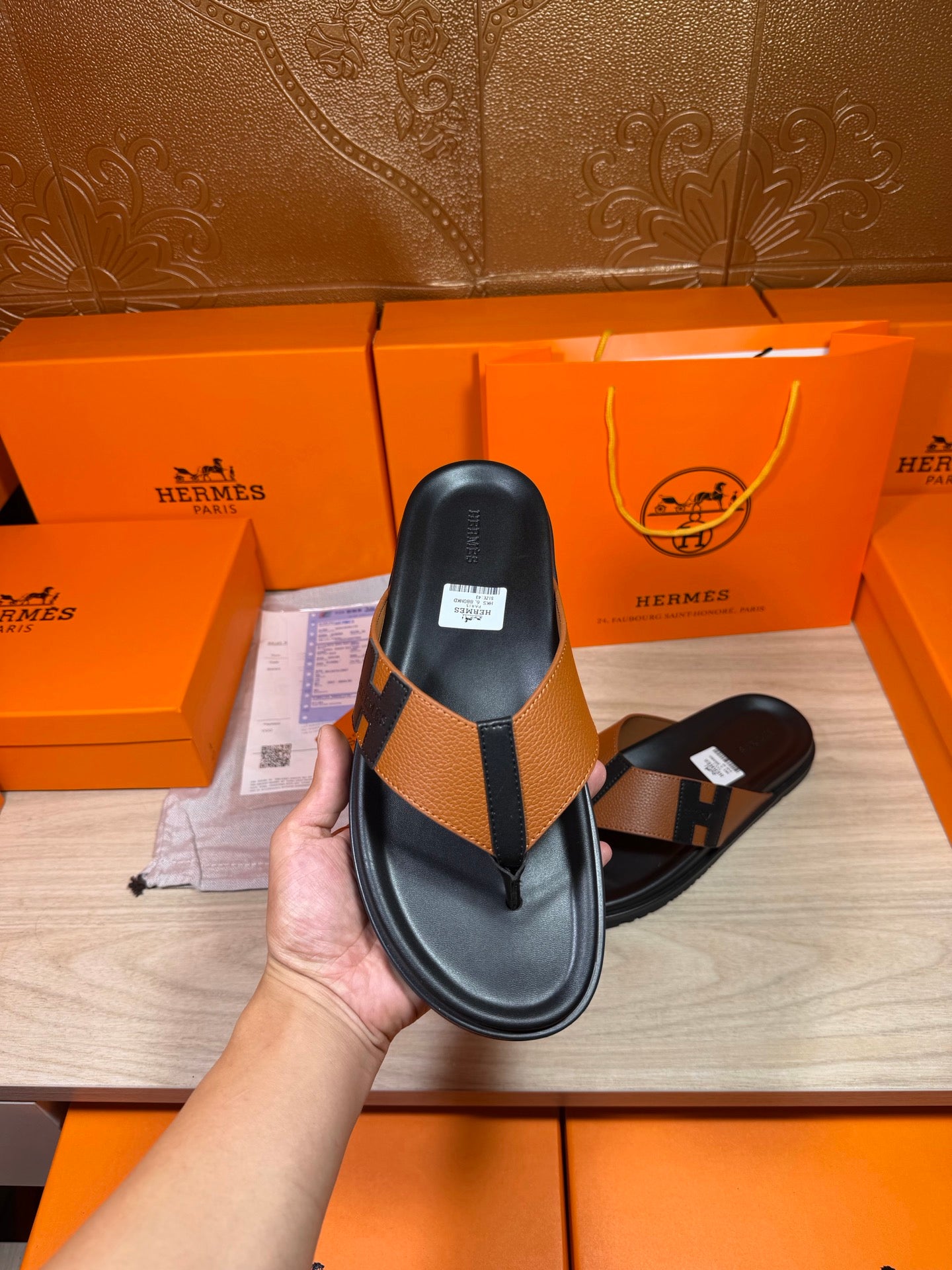Single black thong sandal with tan strap and H buckle detail, held up