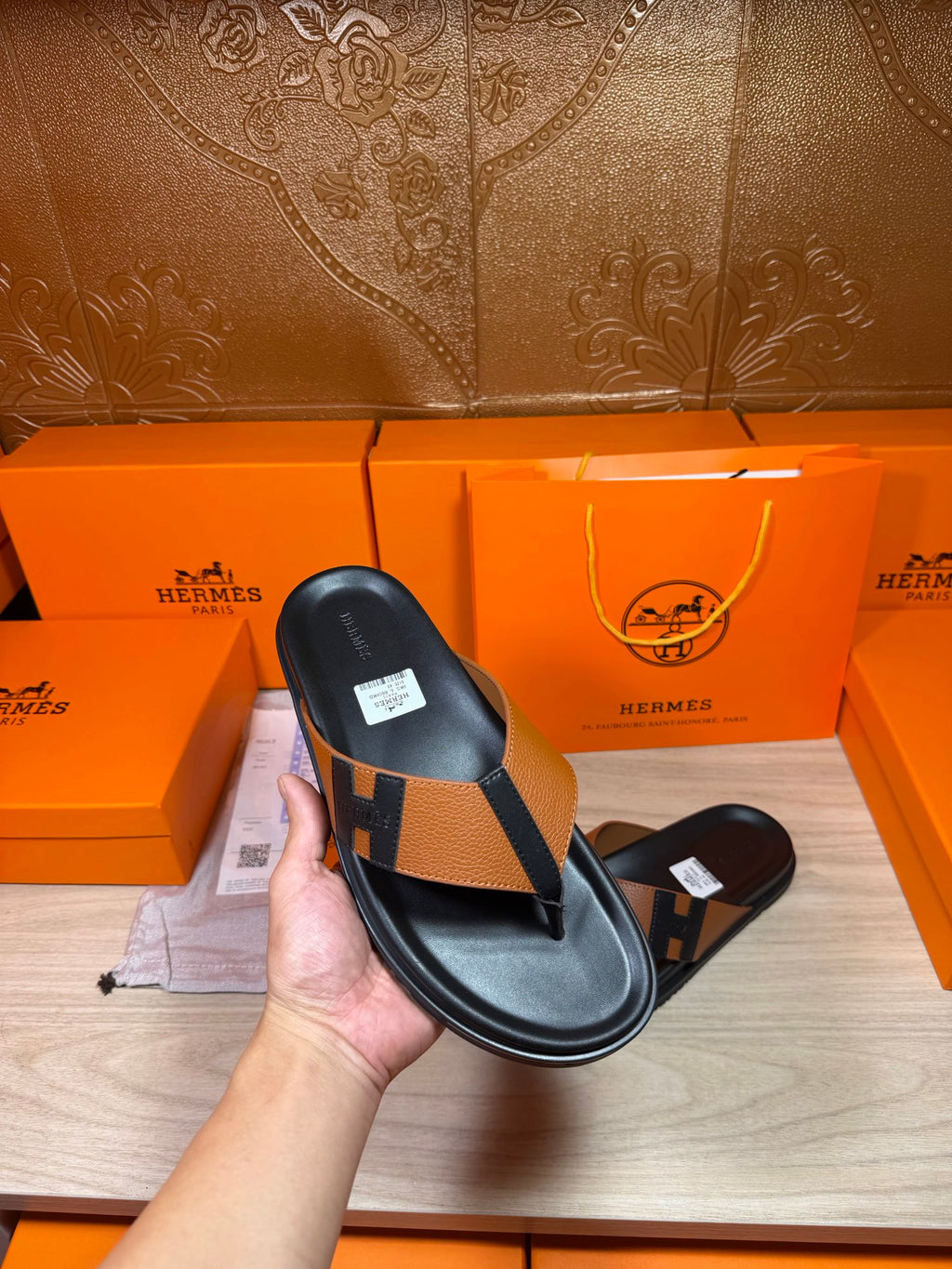 Single black thong sandal with tan strap and H buckle detail, held up