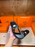 Single black thong sandal with tan strap and H buckle detail, held up